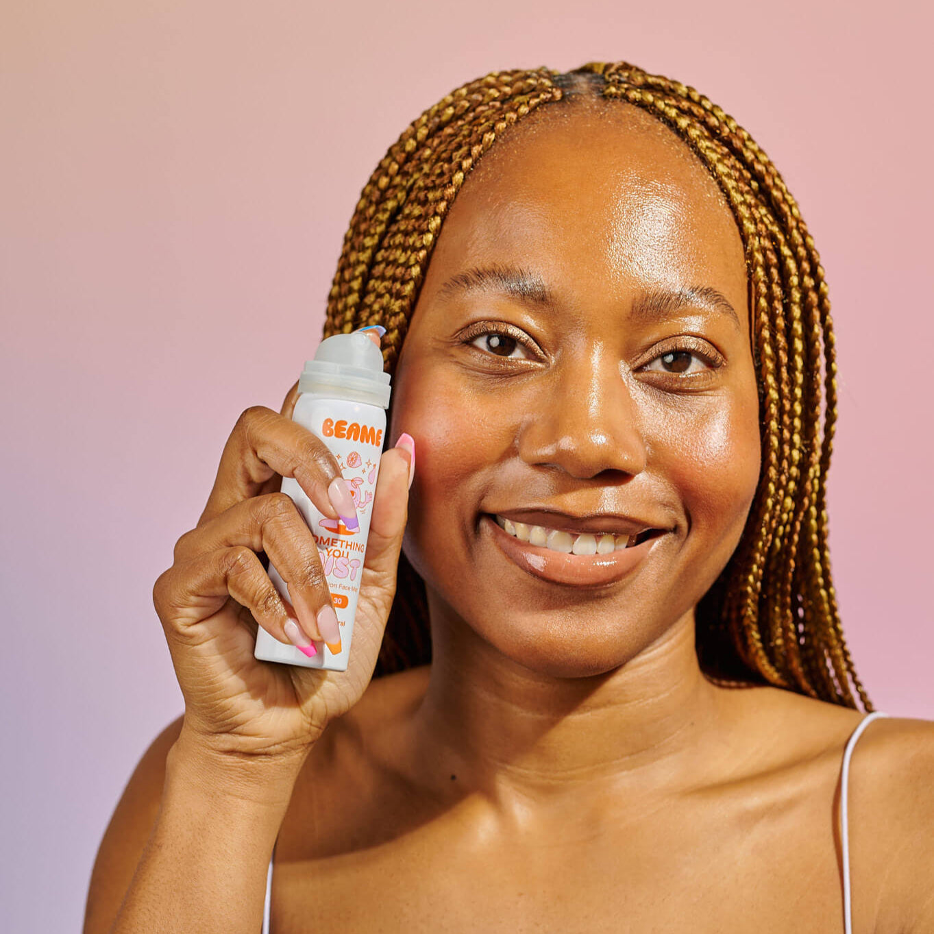 Woman applying sunscreen spray on a pink background