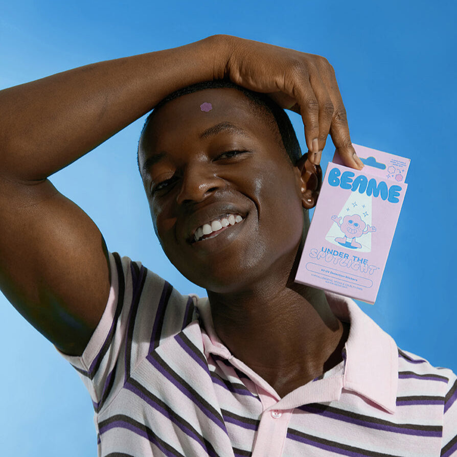 Person holding a BEAME UV SPF sticker pack against a blue background.