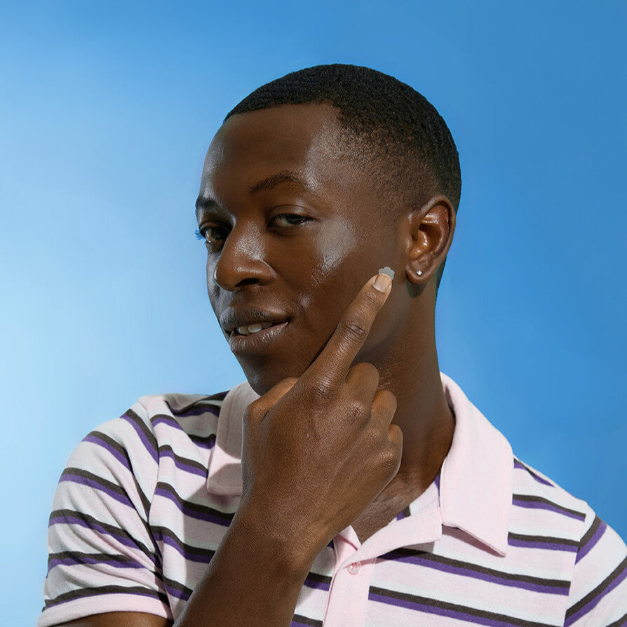 Person wearing a striped shirt against a blue background holding up a BEAME UV SPF sticker.