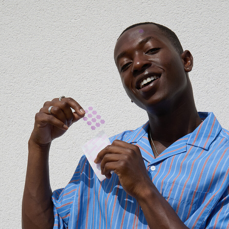 Man in a blue striped shirt holding BEAME UV SPF stickers against a light gray background.